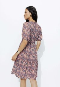 Robe paisley multicolore avec des manches courtes bouffantes, taille élastique et jupe à volants. Tissu lisse avec un motif vivant.