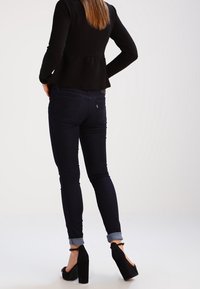 Slimma denimjeans i mörkblått med uppvikta fållar. Matchat med en strukturerad svart peplumtopp och svarta klacksandaler.