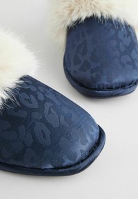 Marineblå slippers med et tekstureret leopardmønster, der har en blød cremefarvet faux fur kant og en polstret sål.