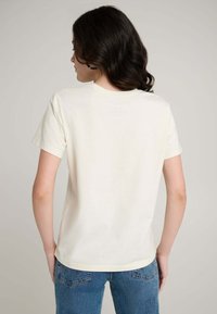 Baumwoll-T-Shirt in Cremefarbe mit kurzen Ärmeln, rundem Ausschnitt und lockerem Schnitt. Rückseite einfarbig ohne sichtbare Logos oder Grafiken.