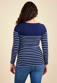 Tumesiniste ja valgete triipudega pikkade varrukatega pluus ümarate kraega, sobiva lõike ja siledast kangast, koos siniste teksadega.