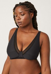 Bralette negra con un pronunciado escote en V, detalles de malla y tirantes ajustables con herrajes metálicos. Tejido suave y forma estructurada.