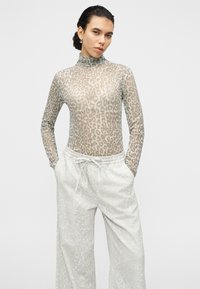 Διαφανές τοπ με μακριά μανίκια σε ανοιχτό μπεζ και καφέ λεοπάρ μοτίβο, με ψηλό λαιμό, σε συνδυασμό με φαρδιά παντελόνια σε ανοιχτό γκρι με το ίδιο μοτίβο.