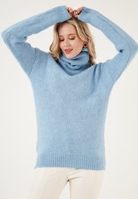 Hellblauer Rollkragensweater aus weichem Strickmaterial, mit langen Ärmeln, gerippten Bündchen und lockerem Schnitt.