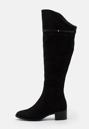 Botte en daim noire montant jusqu'au genou avec un petit talon bloc et un détail de fine lanière près du haut, vue de profil sur fond blanc.