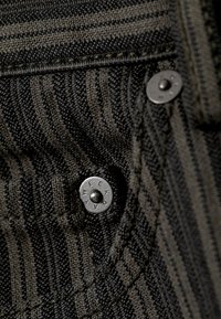 Nærbilde av mørkstripet stoff med to metallknapper merket "WEEKDAY" på en sydd lomme.