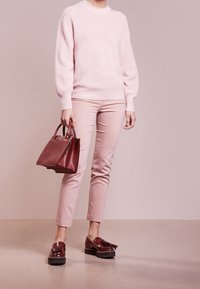 Jasnoróżowy sweter z dzianiny, różowe dopasowane spodnie, bordowa torba o strukturalnym fasonie oraz lakierowane bordowe loafersy z frędzlami i grubą podeszwą.