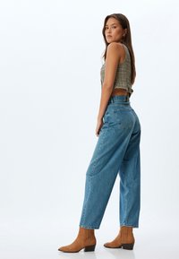 Jeans de mezclilla azul de pierna ancha con una cintura alta, combinados con un top corto de cuadros. Botines de ante marrón con detalles de flecos.