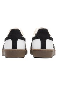 Czarno-białe trampki wykonane z zamszu i skóry, o niskim kroju i teksturowanej, brązowej gumowej podeszwie.