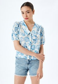 Kurzarm-Hemd aus leichtem Stoff mit blauen Blumen- und Muschelmustern, großem Kragen und gerafften Ärmel-Details.