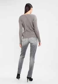 Suéter de punto acanalado gris con escote en V, mangas largas y jeans de mezclilla gris medio. Zapatos de tacón alto negros completan el conjunto.