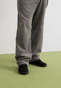 Gray corduroy pants with vertical ridges, relaxed fit, paired with black low-top sneakers. Textured fabric visible along the legs.