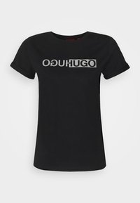 Musta puuvillane T-särk, millel on julge, hõbedane logo kujundus, kus on kirjas "OGUHUGO". Lühikesed rullitud varrukad ja ümar kaelus.