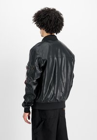 Μαύρο δερμάτινο bomber jacket με ραβδωτό γιακά και μανίκια, με θήκη τσέπης στον ώμο και λείο, γυαλιστερό φινίρισμα.