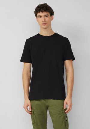 Schwarzes T-Shirt mit kurzen Ärmeln und Rundhalsausschnitt aus Baumwolle, mit regulärer Passform und glatter Textur. Kombiniert mit olivgrünen Cargohosen.