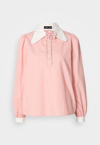 Blusa rosa a maniche lunghe con colletto bianco, caratterizzata da un accento a forma di rosa, chiusura con bottoni e polsini elasticizzati. Realizzata in tessuto leggero.