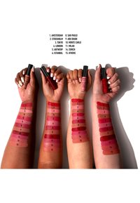 Trois bras présentant des échantillons de rouge à lèvres dans des nuances variées de rouge et de rose, avec des étiquettes numérotées indiquant les noms des couleurs. Des applicateurs en tube noir sont inclus.