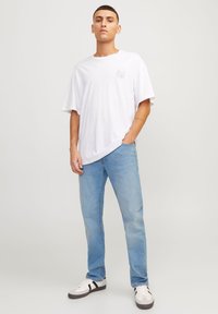Hvit oversized t-skjorte med et lite grafisk design, kombinert med lyseblå jeans og hvite sneakers med svarte aksenter.