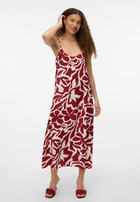 Robe maxi rouge et crème à motifs avec des bretelles fines, présentant un design floral abstrait, une texture lisse et une silhouette décontractée.