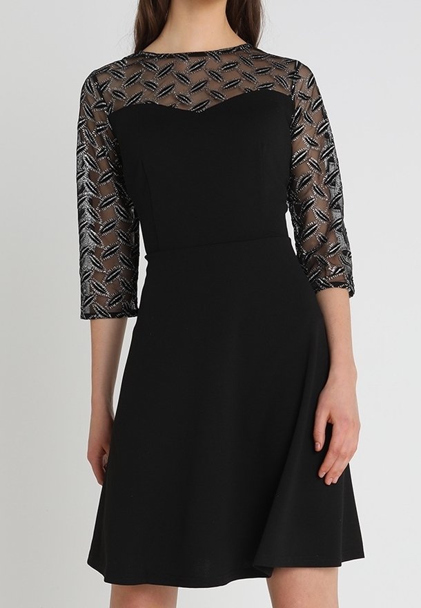 Svart klänning med trekvartslånga ärmar, med en genomskinlig topp med ett geometriskt mönster och en figurnära bodice som vidgar sig vid midjan.