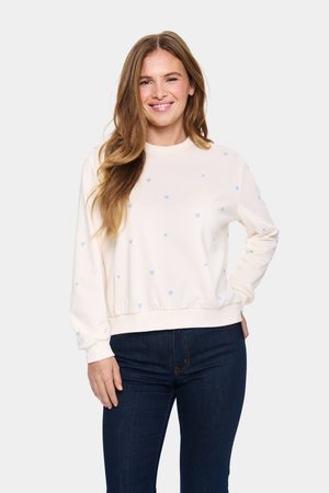 Crème sweatshirt met lichtblauwe hartpatronen, geribde manchetten en onderkant, ontspannen pasvorm, zachte stof, gedragen met donkerblauwe jeans.