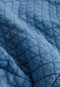 Gequilted denimstof in een middelblauwe tint, met een ruitpatroon en zichtbare stiksels, wat textuur en diepte creëert.