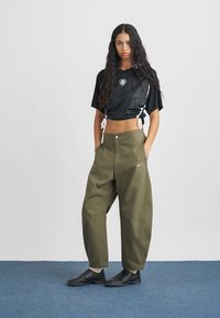 Svart, kort top med nätstil och logotyp; olivgröna, vida byxor; svarta skor; slätt tyg, avslappnad passform med dragsko-detaljer.