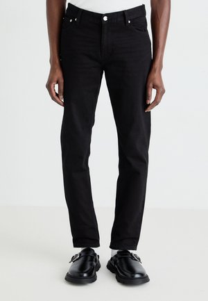 Jeans din denim negru, design ajustat, stil cu cinci buzunare, închidere cu buton și bucle pentru curea. Asortați cu pantofi negri și șosete albe.