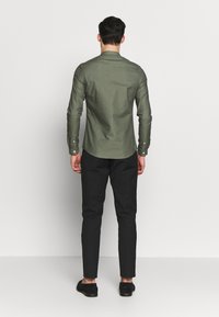 Vihreä nappipaita, jossa on terävä kaulus, kapea malli ja pitkät hihat, yhdistetty kapeisiin mustiin housuihin ja mustiin kenkiin.