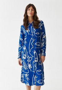 Abito blu con bottoni, caratterizzato da motivi astratti bianchi; maniche lunghe e spacchi laterali, realizzato in un tessuto leggero dalla texture liscia.
