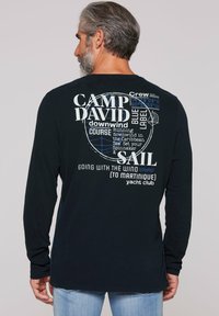 Langearmige marineblauwe T-shirt met witte en blauwe grafische tekst, met nautische thema's en de zinnen "CAMP DAVID" en "SAIL." Gemaakt van katoen.