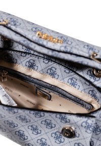 Sac fourre-tout bleu clair avec un tissu à motifs, des accessoires dorés et une poche zippée. L'intérieur révèle une doublure beige avec des étiquettes de marque.