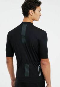 Maillot de cyclisme noir à manches courtes, avec des rayures verticales dans le dos et un logo réfléchissant. Le matériau semble léger et ajusté.