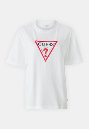 Bílá bavlněná tričko s krátkými rukávy a kulatým výstřihem. Na přední straně má červenou trojúhelníkovou grafiku s nápisem "GUESS" a černým brandingem.