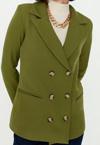 Oliwkowo-zielona dwurzędowa marynarka z wciętymi klapami, dwoma przednimi kieszeniami i złotymi guzikami. Gładka tkanina o dopasowanym kroju.
