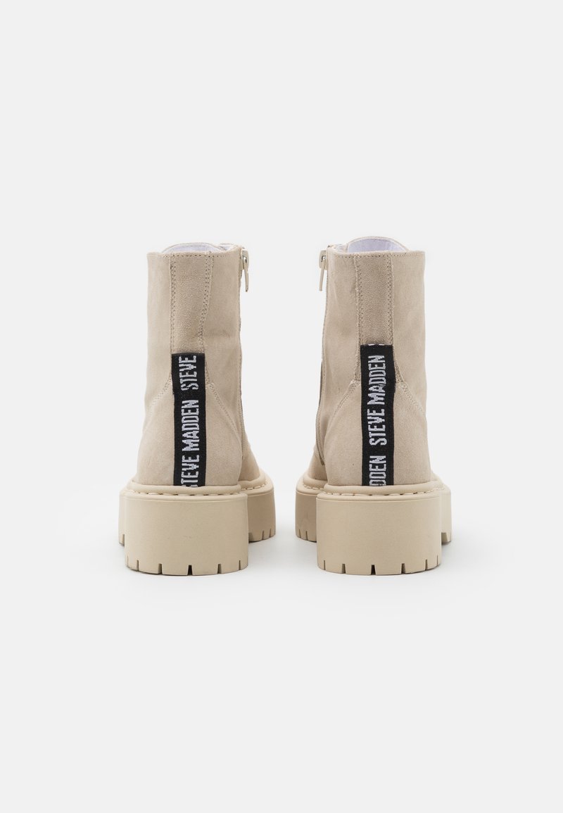 Stivaletti alla caviglia in suede beige con suola piatta chunky e cerniera sul retro, caratterizzati da un'etichetta nera con il nome del marchio.