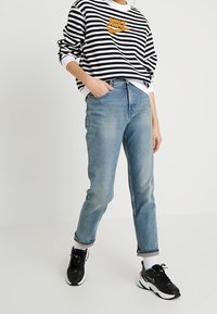 Randig svart och vit sweatshirt med orange logotyp, ljusblå jeans och svarta sneakers. Avslappnad outfit med uppvullade ärmar och en avslappnad passform.