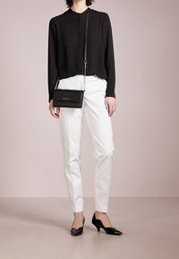 Camisa negra de manga larga con botones, pantalones blancos ajustados, tacones de charol negros y un bolso bandolera negro con una correa de cadena dorada.