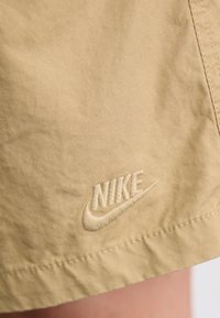 Calções de algodão bege com um logotipo da Nike bordado na bainha, complementados por detalhes de costura visíveis e uma textura suave.