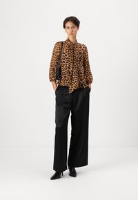 Leoparda raksta bluze ar garām piedurknēm un ar loku detaļu, saskaņota ar augsta vidukļa melniem platā uzvalka biksēm un melniem augstpapēžu zābakiem.