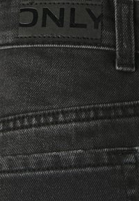 Gros plan sur un jean denim noir montrant une poche arrière et un patch en cuir noir cousu avec le nom de la marque ONLY.