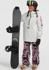 Snowboard con base nera, giacca pullover bianca con logo, pantaloni fantasia rosa e neri, scarponi da snowboard marroni e guanti neri.