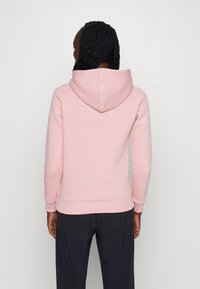 Felpa rosa realizzata in morbido tessuto, con cappuccio aderente, polsini e orlo a coste, e un design semplice senza loghi o motivi visibili.