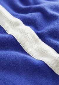 Țesătură albastră cu o suprafață texturată, având o dâră albă țesută. Țesătura are un aspect moale și pufoș, subliniind culoarea și modelul său bogat.