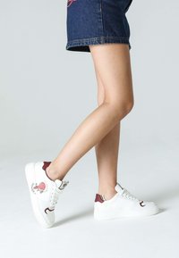 Sneakers i vitt läder med burgundy detaljer, rund tå och strukturerad sula. Hjärtgrafikdetalj på den yttre sidan.