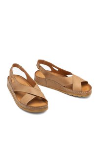 Beżowe skórzane sandały z krzyżującym się paskiem, odkryty tył, teksturowana podeszwa i wycięcia po bokach. Płaska, wyściełana wkładka dla komfortu.