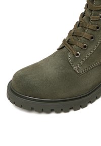 Zaļi zamša potīšu zābaki ar apaļu purngali, gumijas zoli un metāla acīm. Iezīmē kontrastējoša šuvumu un izturīgas auklas, lai nodrošinātu drošu piegulšanu.