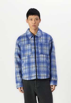 Blue plaid jacket with a zip front, two chest pockets, and a collared neck. Made of a textured fabric with light and dark blue tones.