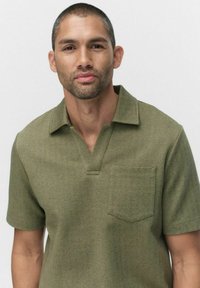 Oliivivärinen lyhythihainen poolopaita, jossa on viisto kaulus, kalanruotokuvio ja rintatasku. Räätälöity malli ja pehmeä kangas.