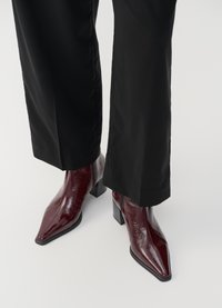 Bordeaux patent leren enkellaarzen met een puntige neus, chunky hak en textuurafwerking, gecombineerd met zwarte wijde broek.